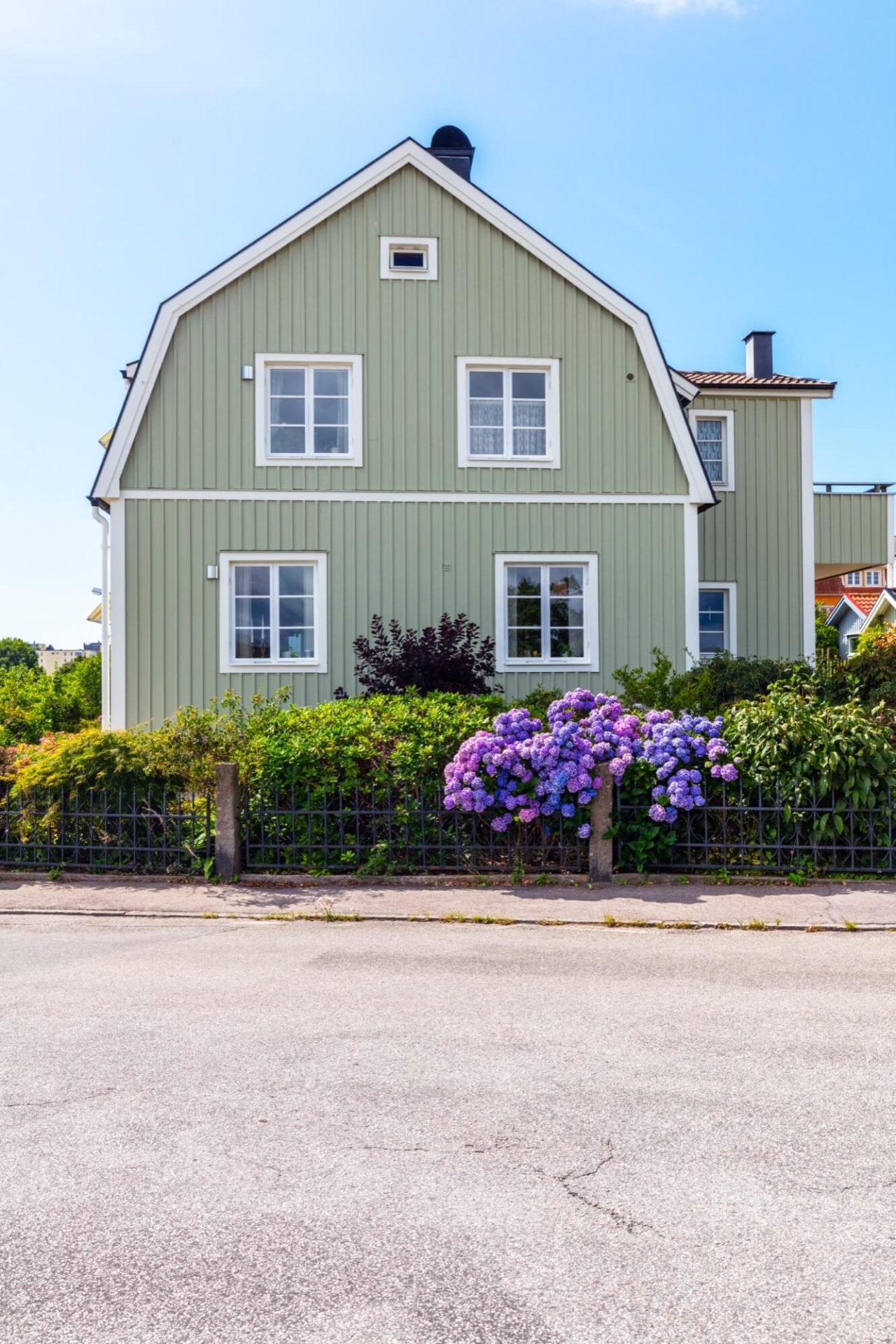 Ett hem omfamnat av grönmålade väggar, vita fasadutsmyckningar, och en trädgård rik på blommande lila hortensior